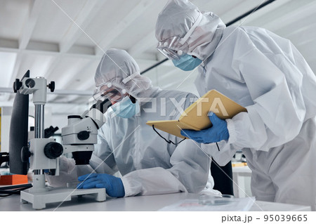 Scientist team, covid research and microscope with team writing notes or results during analysis of a sample in a science and medical lab. Medical researcher in safety suit in biotechnology laborator Scientist team, covid research and microscope with team writing notes or results during analysis of a sample in a science and medical lab. Medical researcher in safety suit in biotechnology laborator 95039665