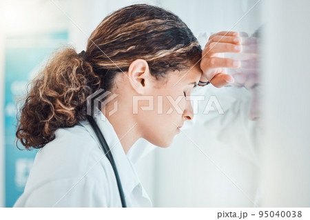 Sad, stress and burnout with doctor against window with headache from healthcare, medical or nurse. Mental health, depression and anxiety with woman working in hospital while tired, fear and fail 95040038