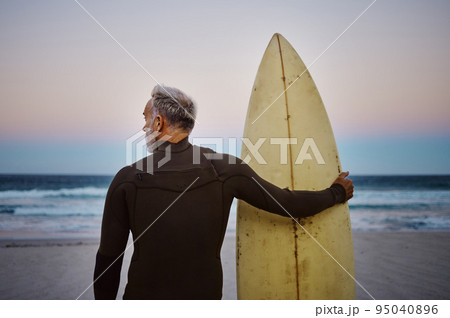 Beach, man and surfboard with back view for morning cardio fitness and tranquil swim in nature. Senior surfer waiting for low tide at ocean for calm surf waves with peaceful sky at dawn. 95040896