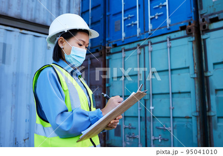 Covid, shipping logistics and employee writing during inspection at a container warehouse. Asian industrial engineer woman with ecommerce notes and planning delivery of cargo with a face mask 95041010