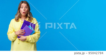 Waist-up portrait of surprised and wondered blonde caucasian female say wow and express amazement hear interesting news, gossiping in college, holding notebooks and essay, blue background Waist-up portrait of surprised and wondered blonde caucasian female say wow and express amazement hear interesting news, gossiping in college, holding notebooks and essay, blue background 95042794