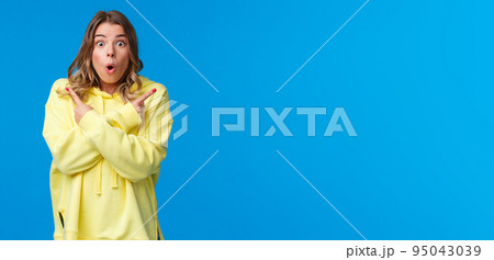 Astonished and excited young blond girl visit awesome place as cant decide what better buy, pointing fingers sideways at left and right product advertisement, look camera ask help with decision 95043039