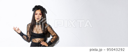 Angry and confused asian woman in witch costume looking bothered by annoying quetion, raising hand up and stare at camera pissed-off. Female at halloween party standing frustrated 95043292