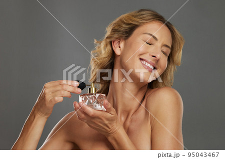 Mature woman, spraying beauty perfume scent and smiling in gray studio background mockup. Bottle of fragrance spray for happy women, self care wellness and luxury cosmetic product for body wellbeing 95043467