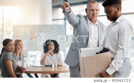 Black man, sad and fired by boss in a meeting holding a box in disappointment at the office. Manager or company leader pointing to the exit and firing employee in front of colleagues at the workplace 95043723