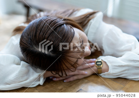 テーブルにうつ伏せで寝る若い女性 95044028