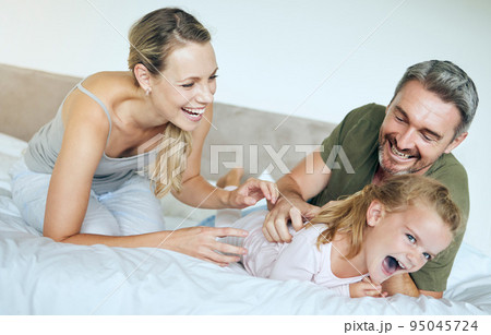 Happy family, bed and fun family playing and laughing while relaxing with little girl in a bedroom. Happy, playful and loving parents being silly with excited child, enjoying free time in their home Happy family, bed and fun family playing and laughing while relaxing with little girl in a bedroom. Happy, playful and loving parents being silly with excited child, enjoying free time in their home 95045724