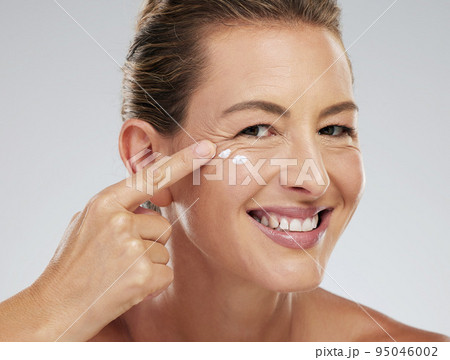 Mature model, skincare and cream on face for beauty, health and happiness with studio background. Woman, skin and happy for anti aging product for facial, cosmetic and wellness in portrait with smile 95046002