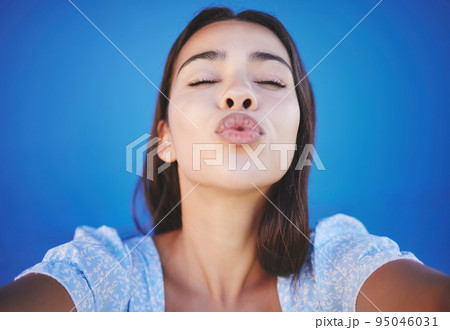 Woman face, blowing kiss and selfie portrait blue background for love emoji, relax and flirting on social media. Young girl beauty lips, mouth and funny expression of joy, happiness or summer style 95046031