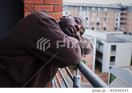 Depression in covid pandemic with a sad man suffering from mental illness, lonely while outside on a balcony. Unhappy male feeling hopeless and annoyed, frustrated with compliance and corona rules 95046445