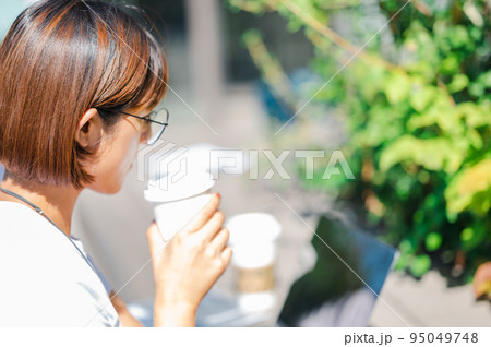 テラスでコーヒーを飲みながらパソコンを見る女性 95049748