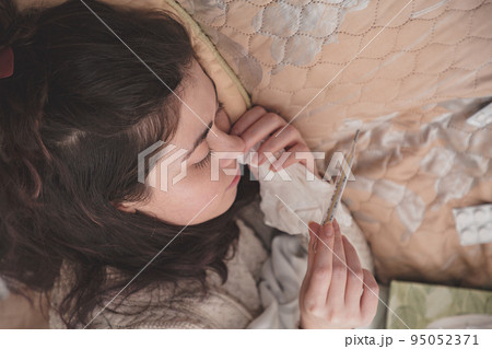 sick girl in bed looking at thermometer sick girl in bed looking at thermometer 95052371