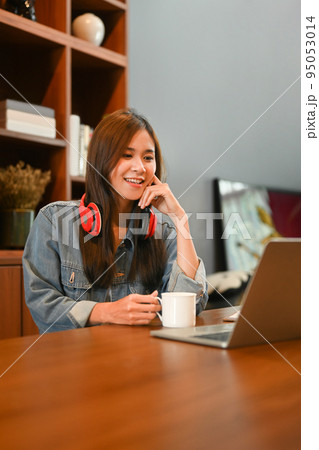 Beautiful stylish woman with headphone using laptop computer on wooden desk in home office 95053014