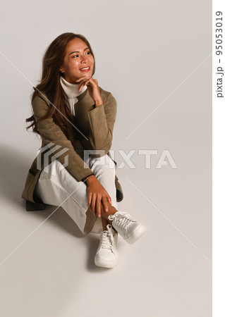 Gorgeous young woman in stylish autumn outfits sitting over white studio background Gorgeous young woman in stylish autumn outfits sitting over white studio background 95053019