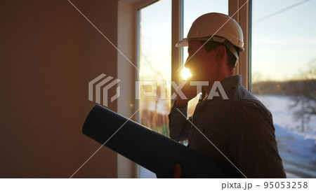 builder silhouette. business building concept. worker in a helmet silhouette idea concept. an engineer in a hard lifestyle hat stands at the window in the house inside the construction site. 95053258