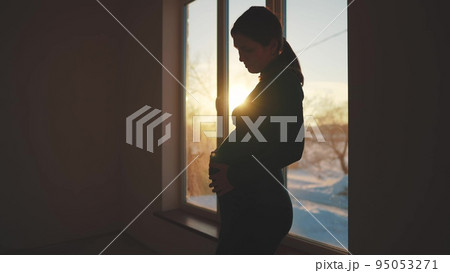 woman pregnant. motherhood a pregnancy concept. 40 year old pregnant woman stands in a dress by the window sunlight holding her stomach silhouette. silhouette of a girl in by the window 95053271