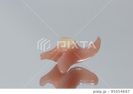 Plastic artificial false unit tooth. Dental prosthesis close-up on a blue background. Dentistry conceptual photo. Prosthetic dentistry. False teeth 95054697