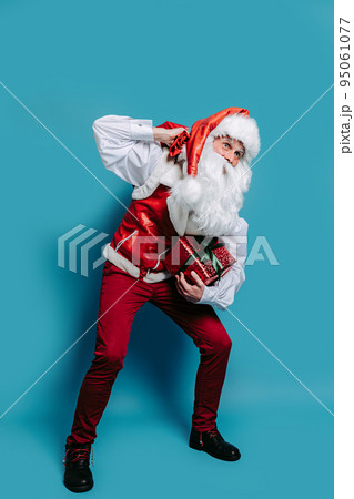 Full size of santa claus who sat down holding heavy sack of gifts on shoulder holds gift box in hand 95061077