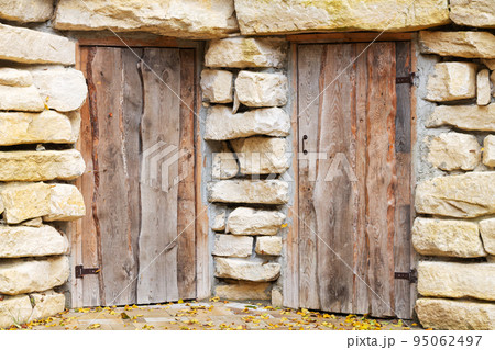 Closed ancient doors in rough stone wall 95062497