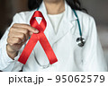World aids day and national HIV AIDS and ageing awareness month with red ribbon on medical or surgical doctor's hand 95062579