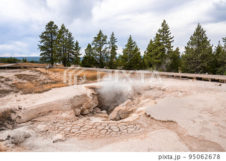 Smoke emitting from geyser at Fountain Paint Pots. Hot spring amidst forest in Yellowstone national park. Famous geothermal landscape with cloudy sky in background. 95062678