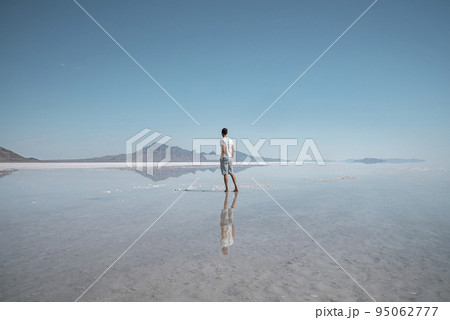 Man sightseeing Bonneville salt flat and mountains. Tourist exploring beautiful peak reflecting in water with clear sky in background. He is spending leisure time during summer vacation. 95062777