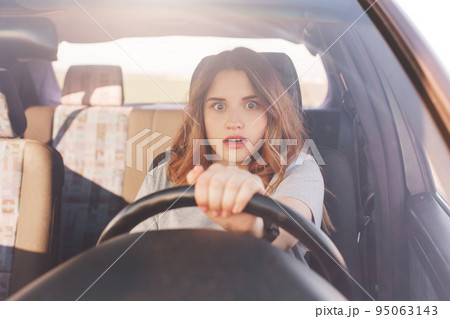 Terrified young cute female looks with depressed scared expression in front as drives car, has collision with other transport or accident on road, being inexperienced driver. Problems on road Terrified young cute female looks with depressed scared expression in front as drives car, has collision with other transport or accident on road, being inexperienced driver. Problems on road 95063143