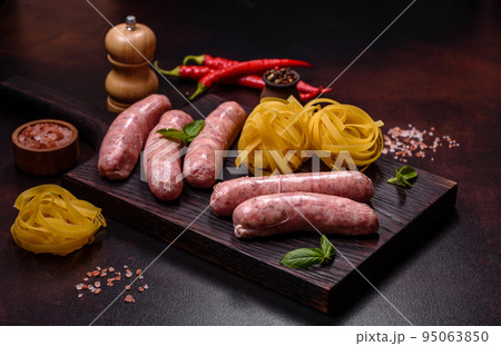Raw sausages with ingredients on a cutting board on a dark concrete background with copy space Raw sausages with ingredients on a cutting board on a dark concrete background with copy space 95063850