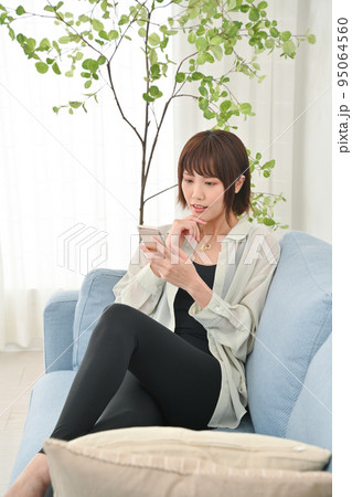 ソファーに座ってスマホの操作をする女性 95064560