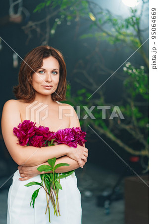 an attractive gentle woman with bare shoulders and arms with a peonies. 95064669