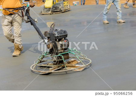 In a construction site, a worker polishes and levels a cement screed mortar floor as part of the construction process 95066256