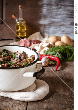 Dish of potatoes with mushrooms on a wooden background and raw ingredients. 95067339