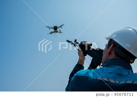 Caucasian man in a helmet shoots a flying drone with a rifle. Caucasian man in a helmet shoots a flying drone with a rifle. 95070711