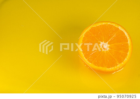 Water falling from orange hue orange on yellow background. Orange slice and water splashing, drops of juice falling from juicy fruit. Making cocktail of fruits, drinking cold lemonade 95070925