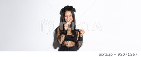 Image of thoughtful smiling asian woman in halloween outfit have an idea, holding credit card and looking cunning at upper left corner 95071567