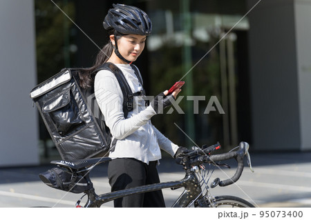 スマホを手に持ってロードバイクを引いているフードデリバリー 女性配達員 スマホを手に持ってロードバイクを引いているフードデリバリー 女性配達員 95073400