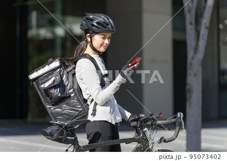 スマホを手に持ってロードバイクを引いているフードデリバリー　女性配達員 95073402