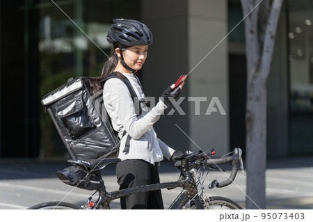スマホを手に持ってロードバイクを引いているフードデリバリー 女性配達員 スマホを手に持ってロードバイクを引いているフードデリバリー 女性配達員 95073403