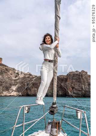 Woman standing on the nose of the yacht at a sunny summer day, breeze developing hair, beautiful sea on background 95076329