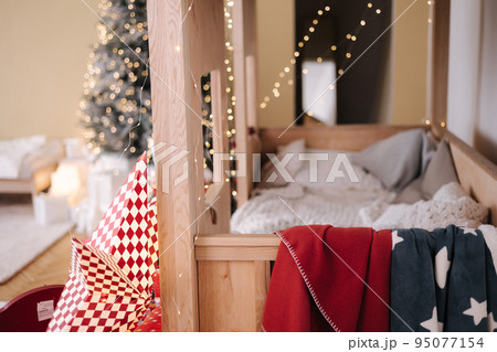 Children room with Christmas decorations. Presents in red festive packaging. Interior design for kids. Background of christmas tree lights Children room with Christmas decorations. Presents in red festive packaging. Interior design for kids. Background of christmas tree lights 95077154