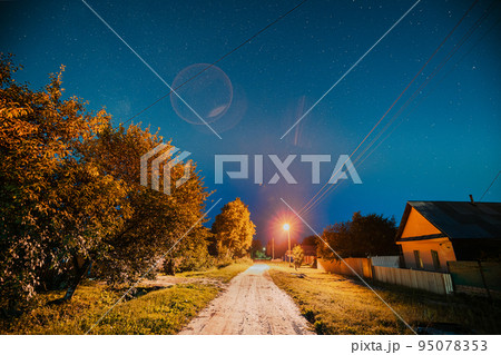 Night sky over street with houses in village. Night starry sky above village with bright stars and meteoric track trail. Glowing stars above summer nature 95078353