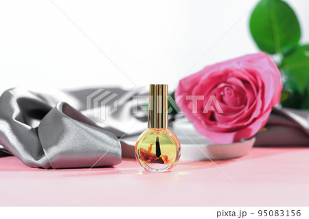 cuticle massage oil with rose petals infusion. pink rose flower next to a bottle of nail care oil, hans and nails beauty care, skin moisturizing and nourishing, spa manicure concept. cuticle massage oil with rose petals infusion. pink rose flower next to a bottle of nail care oil, hans and nails beauty care, skin moisturizing and nourishing, spa manicure concept. 95083156