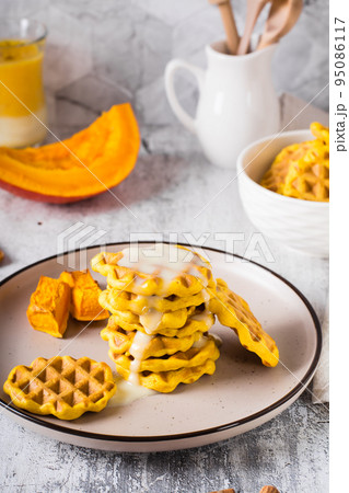 A stack of pumpkin waffles with sweet sauce on a plate on the table. Homemade baking. Vertical view A stack of pumpkin waffles with sweet sauce on a plate on the table. Homemade baking. Vertical view 95086117
