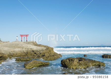 伊豆白浜海岸、大明神岩の鳥居で撮影をする観光客と水しぶきに浮かぶ虹 95086158