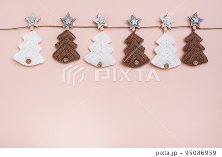 Christmas handmade. Knitted fir-trees in a row on a rope on a pastel background. Handicraft and leisure. Copy space 95086959