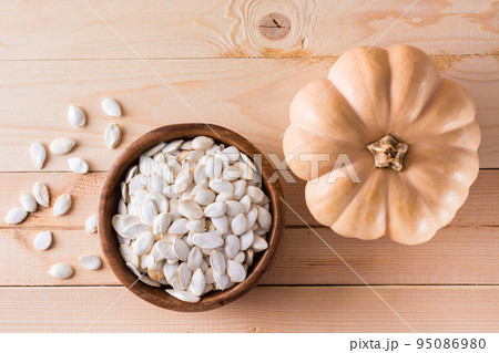 Roasted pumpkin seeds in a plate and pumpkin on a wooden table. Top view 95086980