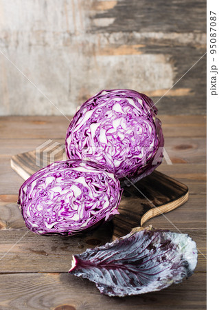 A head of red cabbage cut in half on a cutting board on a wooden table. Vertical view A head of red cabbage cut in half on a cutting board on a wooden table. Vertical view 95087087