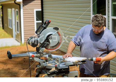 In order to connect wooden boards for construction work, the carpenter is using a screwdriver to drill holes in the boards. 95089152