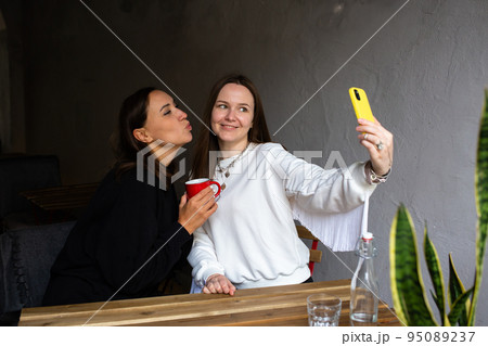 Two women friends have fun outdoors in cafe and take a selfie on a smartphone 95089237