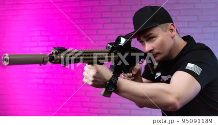 a male special agent with an automatic airsoft rifle on a neon background a male special agent with an automatic airsoft rifle on a neon background 95091189